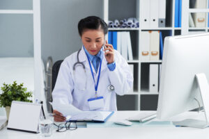 Asian medical specialist sitting at her table and calling to patient